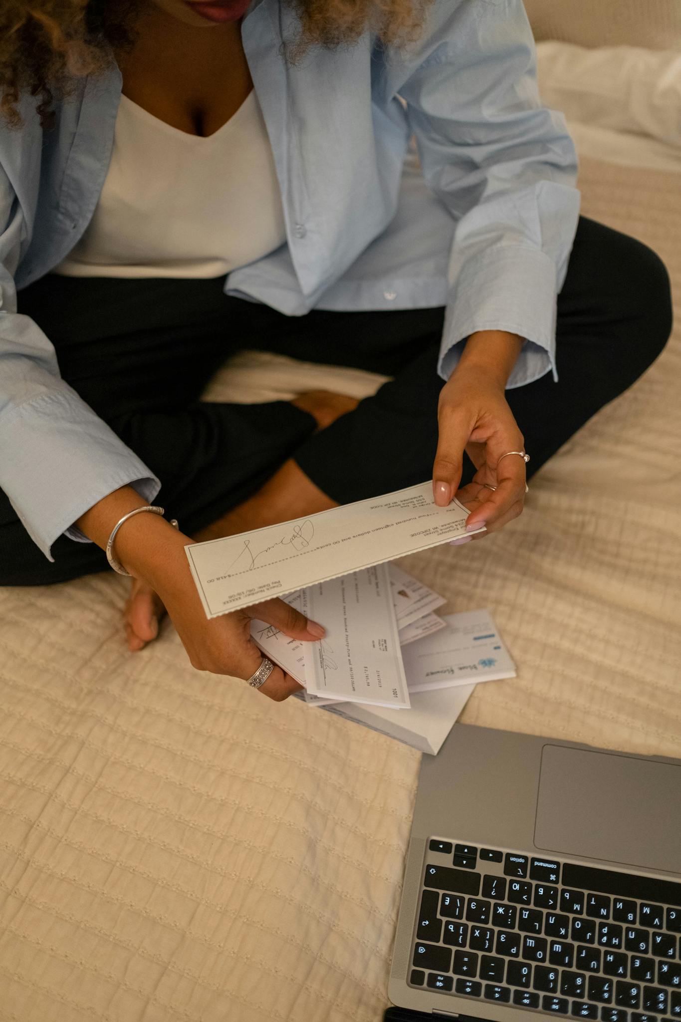 Individual sitting cross-legged examining papers near laptop indoors.